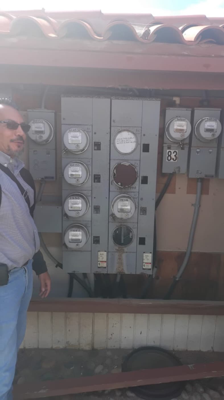 Resident standing next to a panel of electrical meters in one of the community módulos